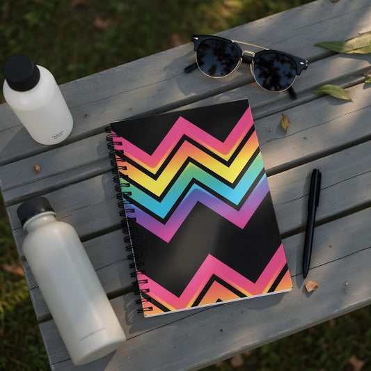 Spiral notebook with black cover featuring a rainbow zigzag pattern and items on a wooden table.