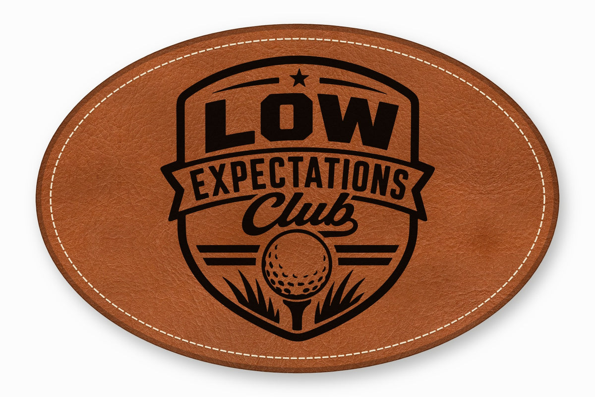Oval brown leather patch with white stitched border, featuring a black Low Expectations Club golf logo.
