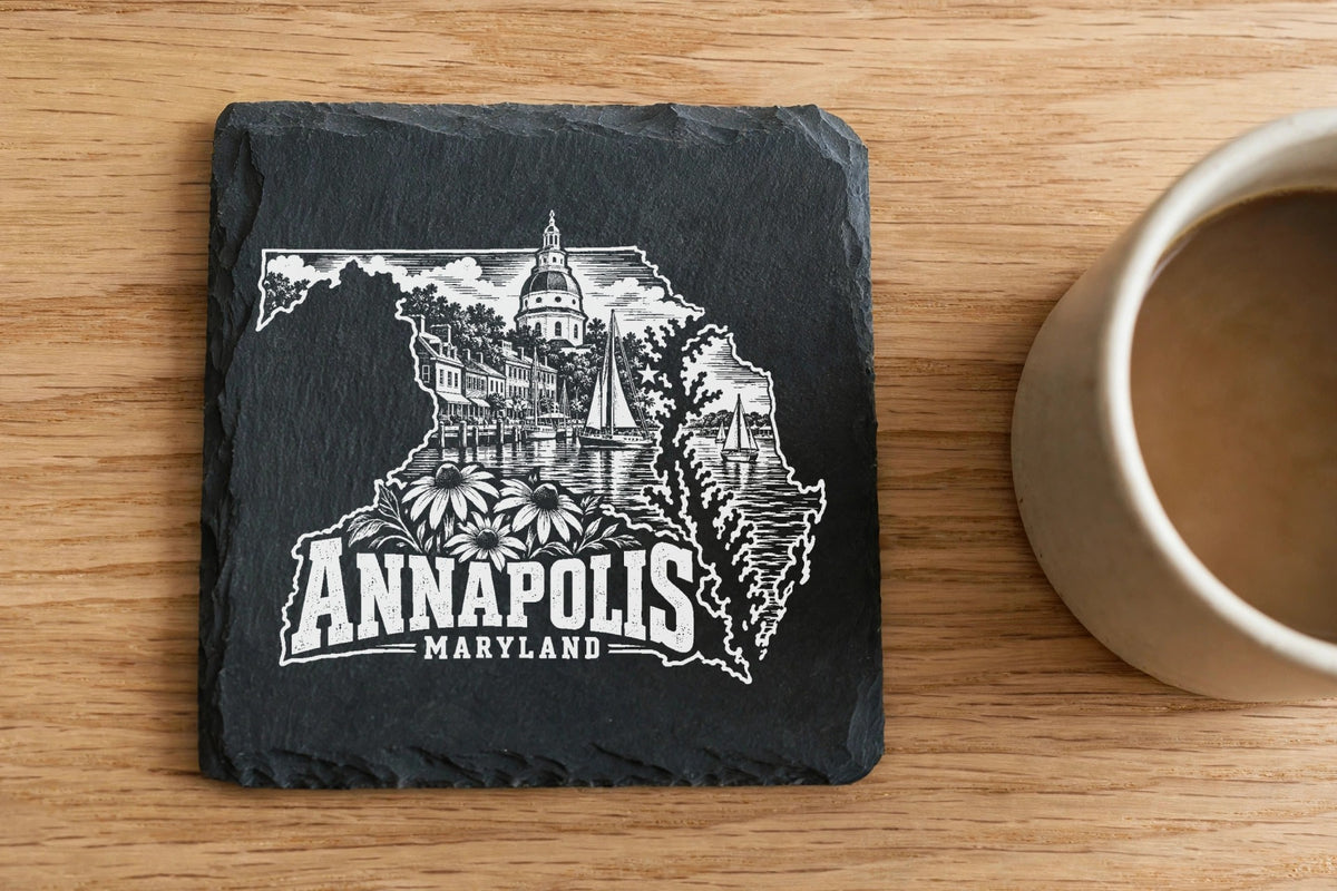 Square black slate coaster engraved with a white Annapolis, Maryland skyline design next to a coffee mug on wood.