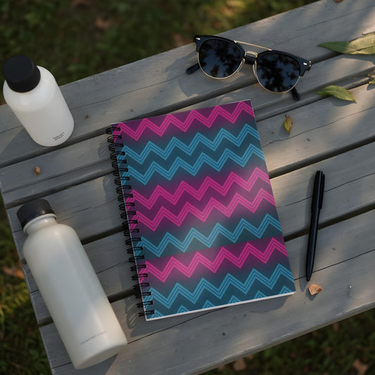 Spiral notebook with pink and blue zigzag pattern on dark background.