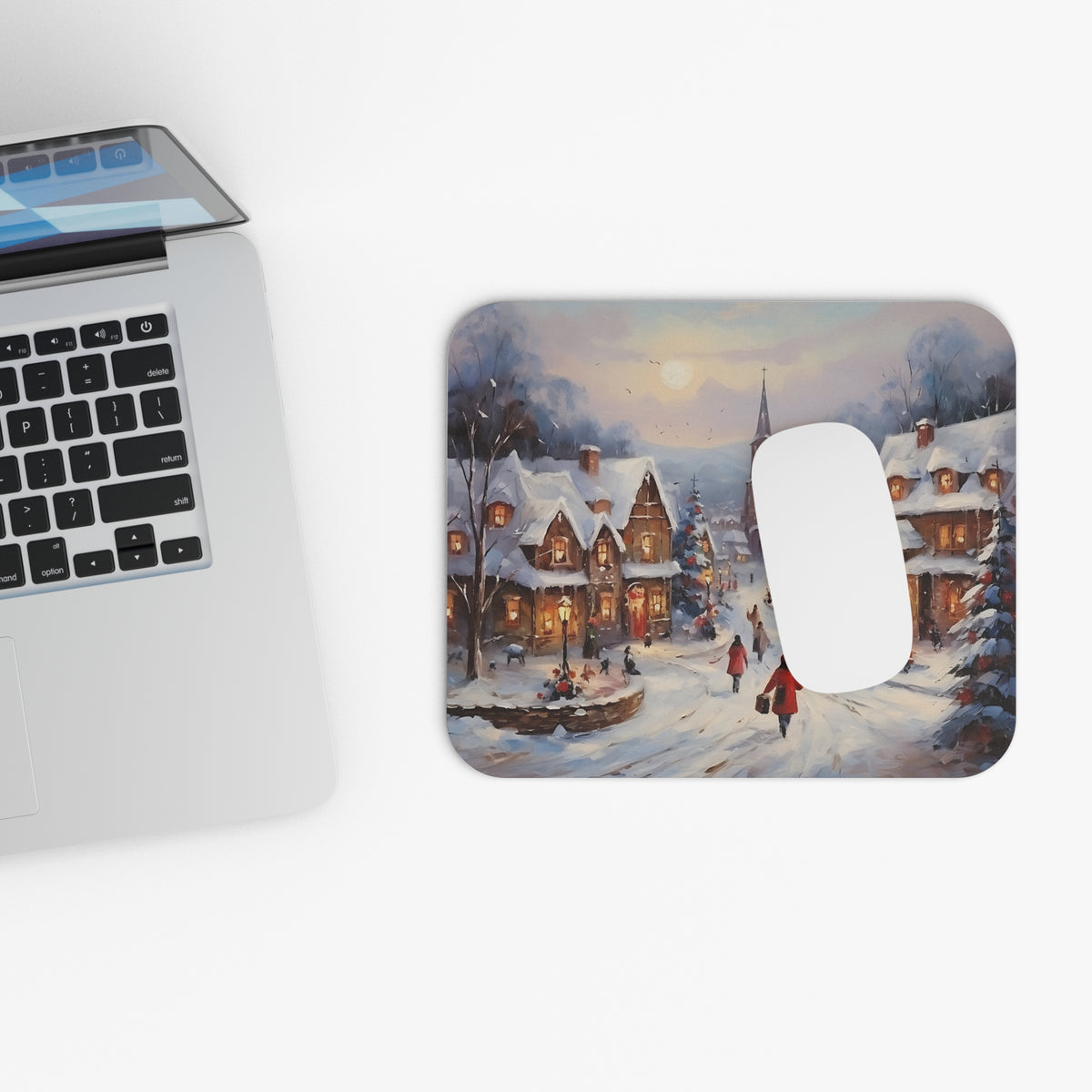 Mousepad with a snowy village painting, featuring a laptop and a white mouse.