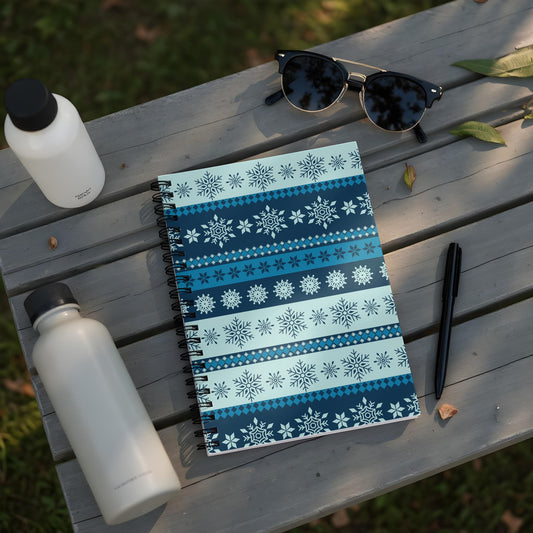 Spiral notebook with blue snowflake pattern, sunglasses, pens, and water bottles on a wooden surface.