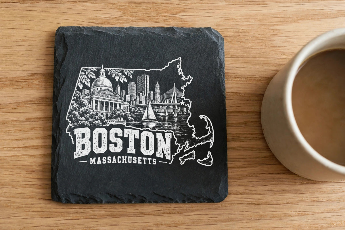 A square black slate coaster engraved with a Boston, Massachusetts cityscape design on a wooden table.