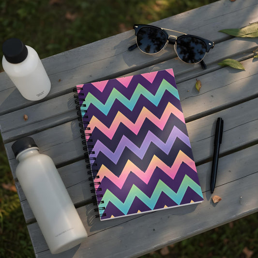 Spiral notebook with multicolor chevron pattern, water bottles, sunglasses, and pen on a wooden bench.