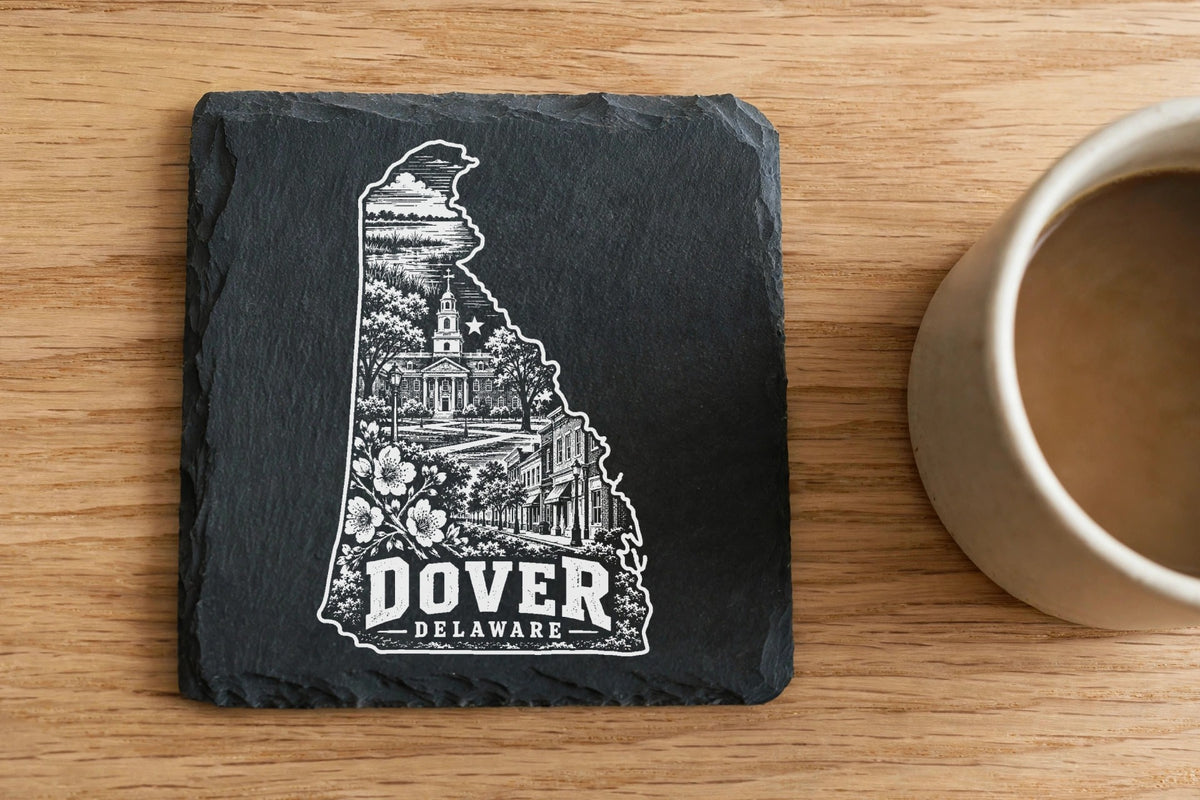 Square slate coaster engraved with a map of Delaware containing Dover landmarks next to a coffee mug.