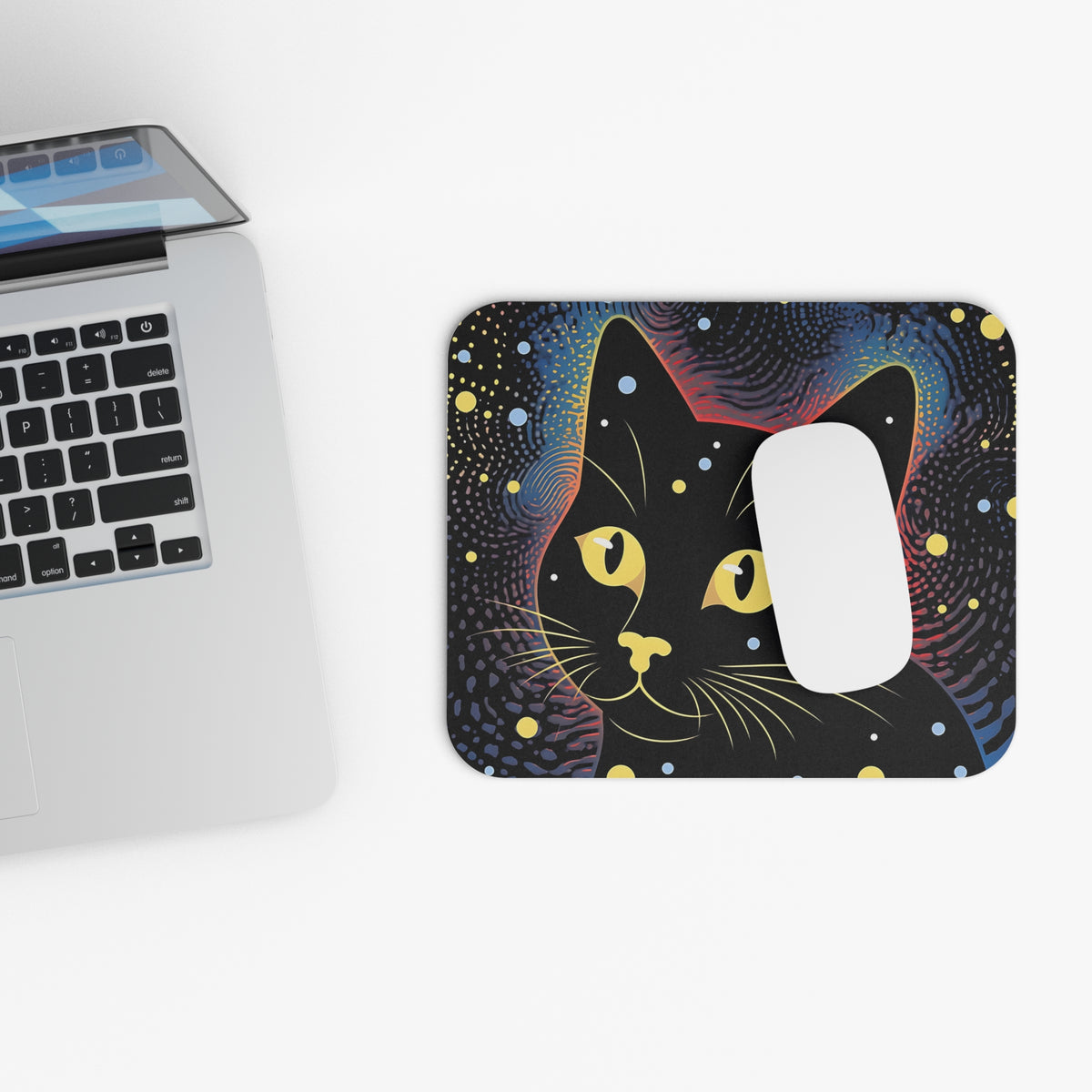 A white mouse rests on a rectangular mouse pad featuring a black cat against a colorful, starry night sky backdrop beside a laptop.