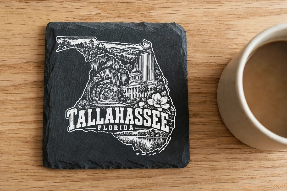 Square black slate coaster engraved with a Tallahassee, Florida design beside a coffee mug.