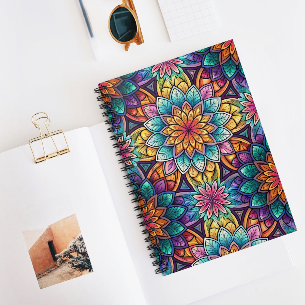 Spiral notebook with vibrant mandala pattern cover on white desk.