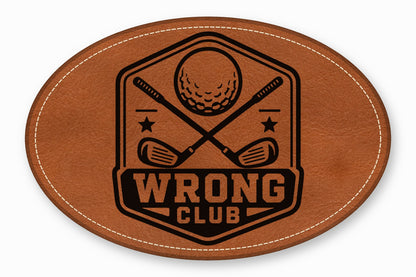 An oval brown leather patch with white stitched border featuring a black golf emblem and text reading WRONG CLUB.