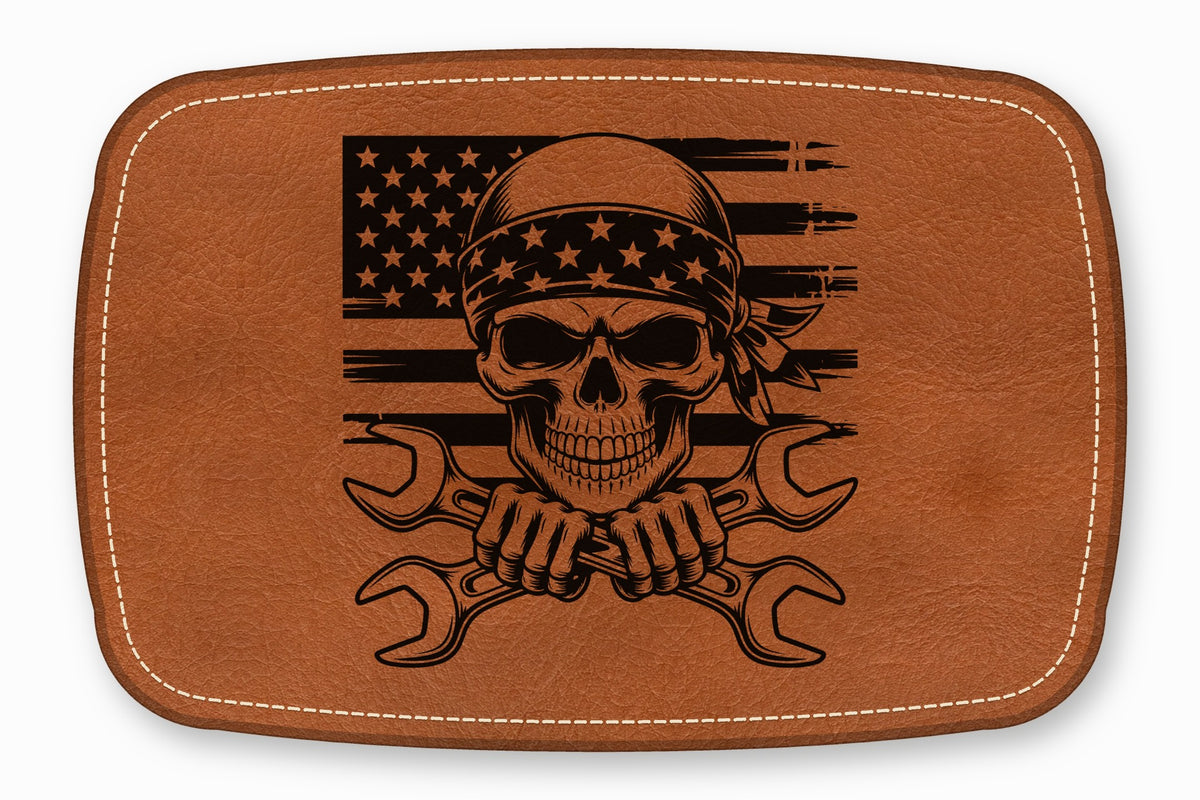 Brown rectangular leather patch with rounded corners, white perimeter stitching, and a skull wearing a bandanna over crossed wrenches and an American flag.