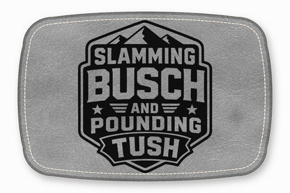 Gray leather patch with rounded corners, white stitching, and a black mountain emblem reading Slamming Busch and Pounding Tush.