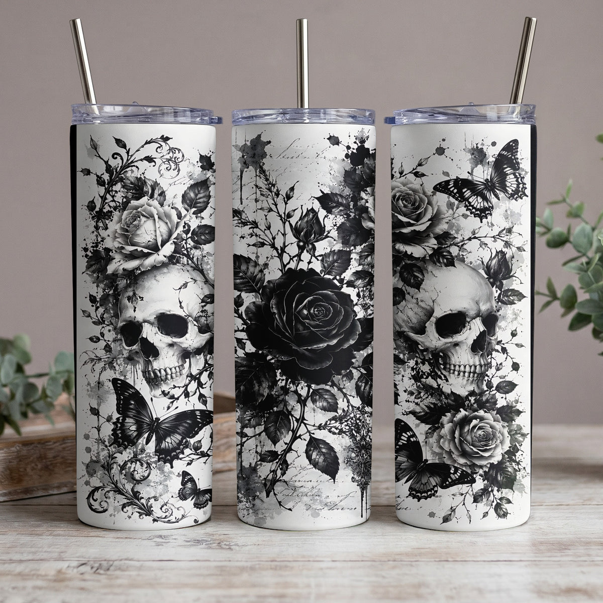 Three tumblers with black and white skull, rose, and butterfly designs.