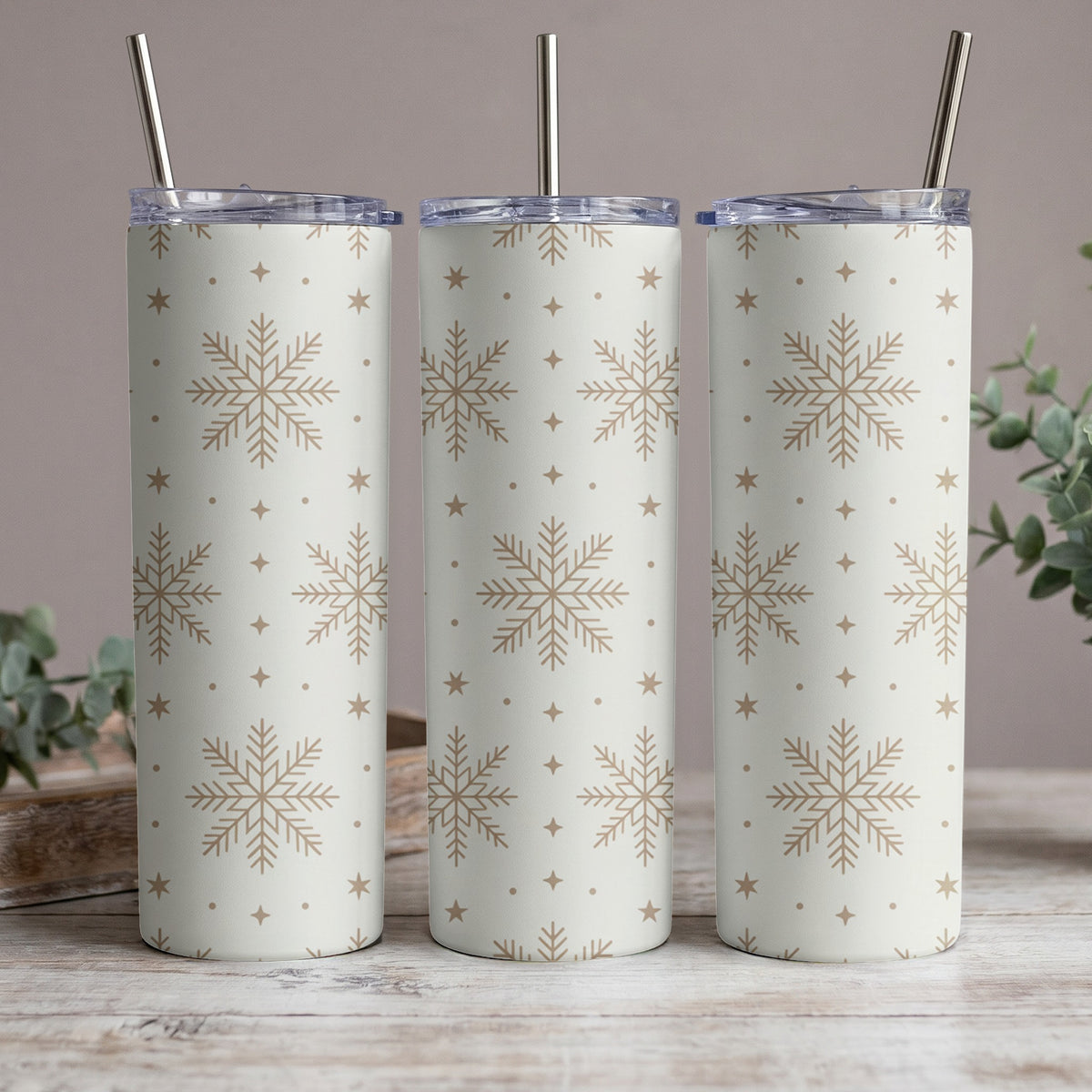 Three white tumblers with gold snowflakes and stars pattern, each with a metal straw.