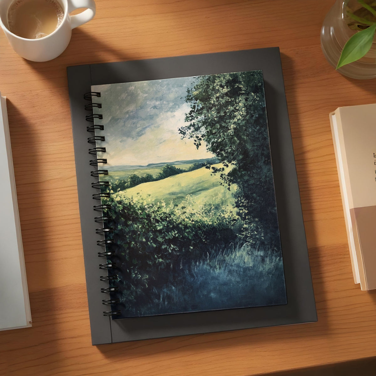 Spiral notebook with a landscape painting of rolling green hills and trees.