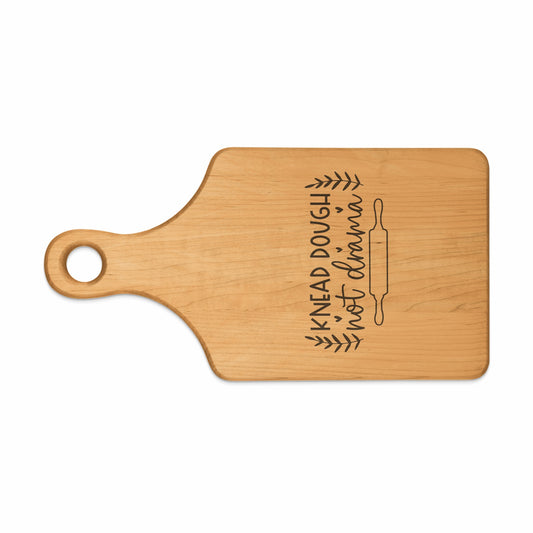 Wooden cutting board with "Knead Dough, Not Drama" and rolling pin design.