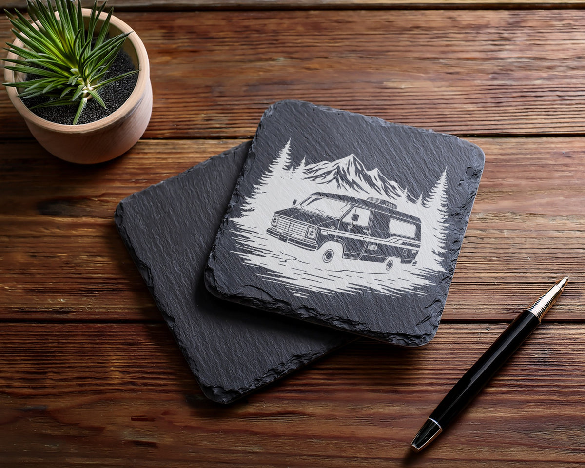 Slate coaster with etched RV, mountains, and trees, next to pen.