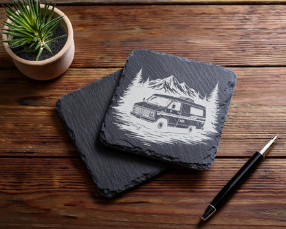 Slate coaster with etched RV, mountains, and trees, next to pen.