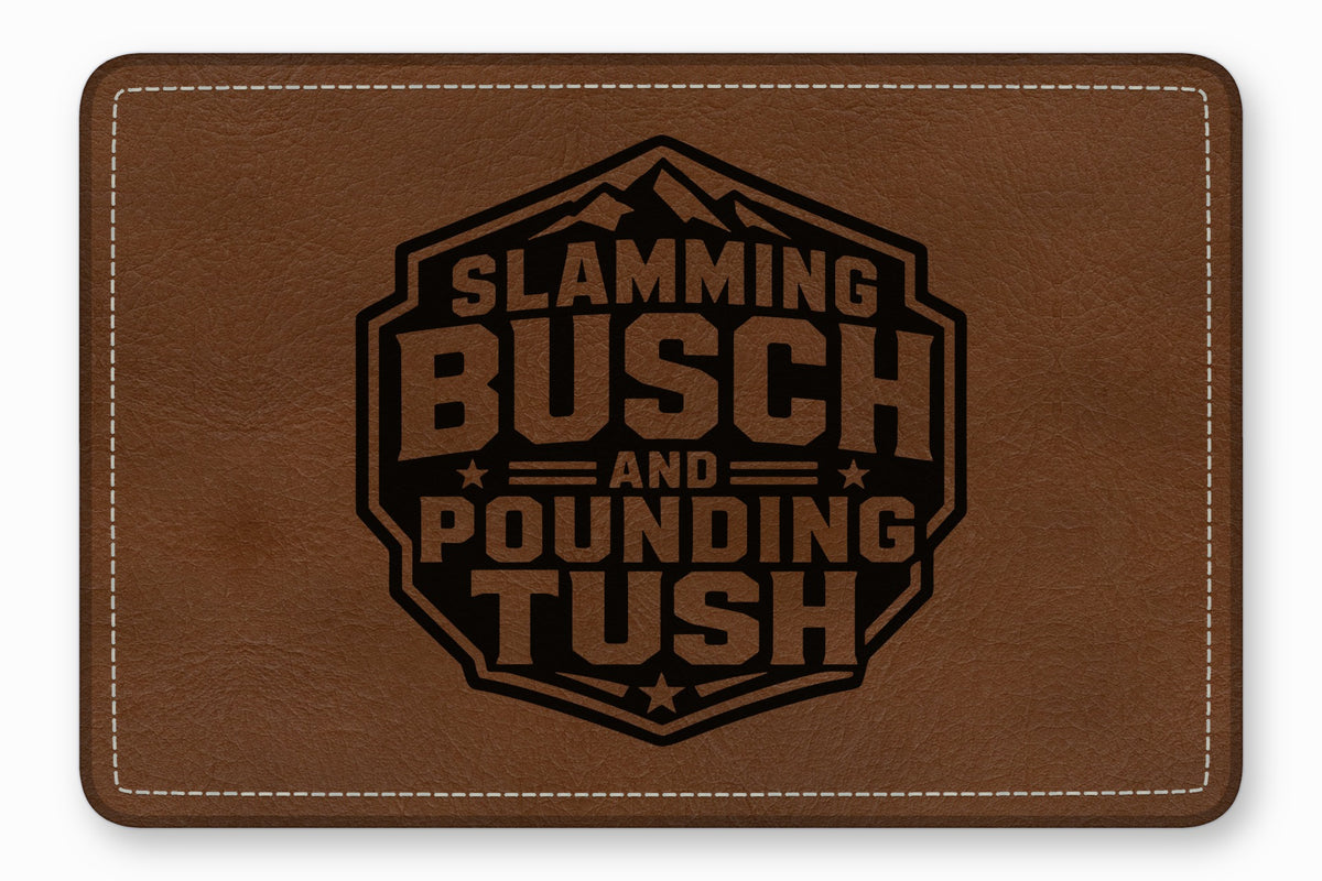 Brown leather patch with white stitching and a black engraved mountain logo featuring the text Slamming Busch and Pounding Tush.