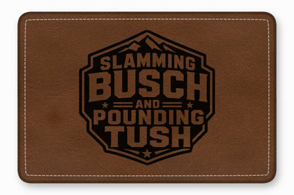 Brown leather patch with white stitching and a black engraved mountain logo featuring the text Slamming Busch and Pounding Tush.