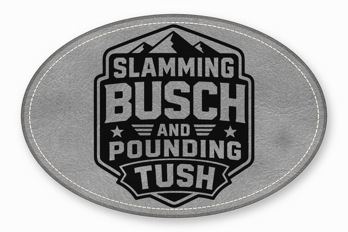 An oval grey leather patch featuring a black badge with mountains and the text Slamming Busch and Pounding Tush.