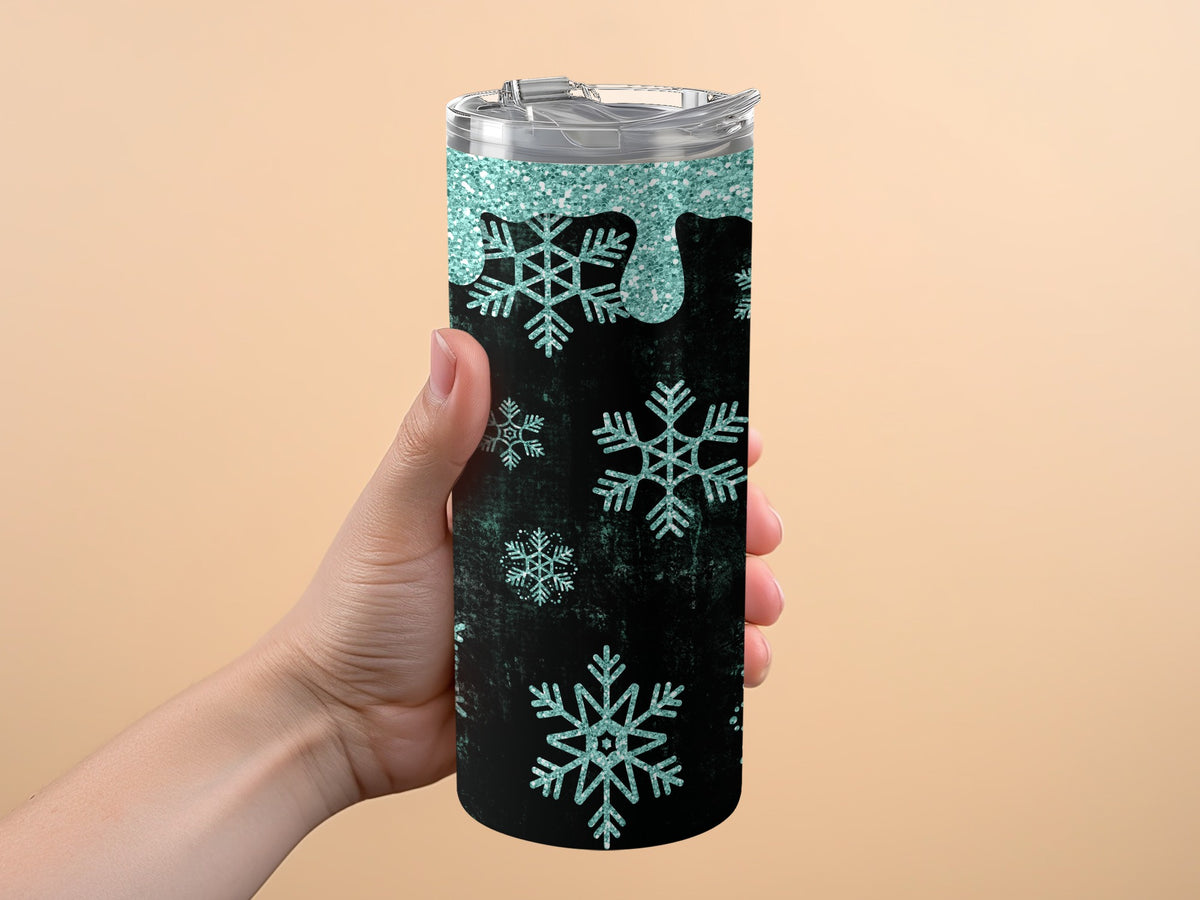 Tumbler with teal glitter drips and snowflakes on black background, held by a hand.