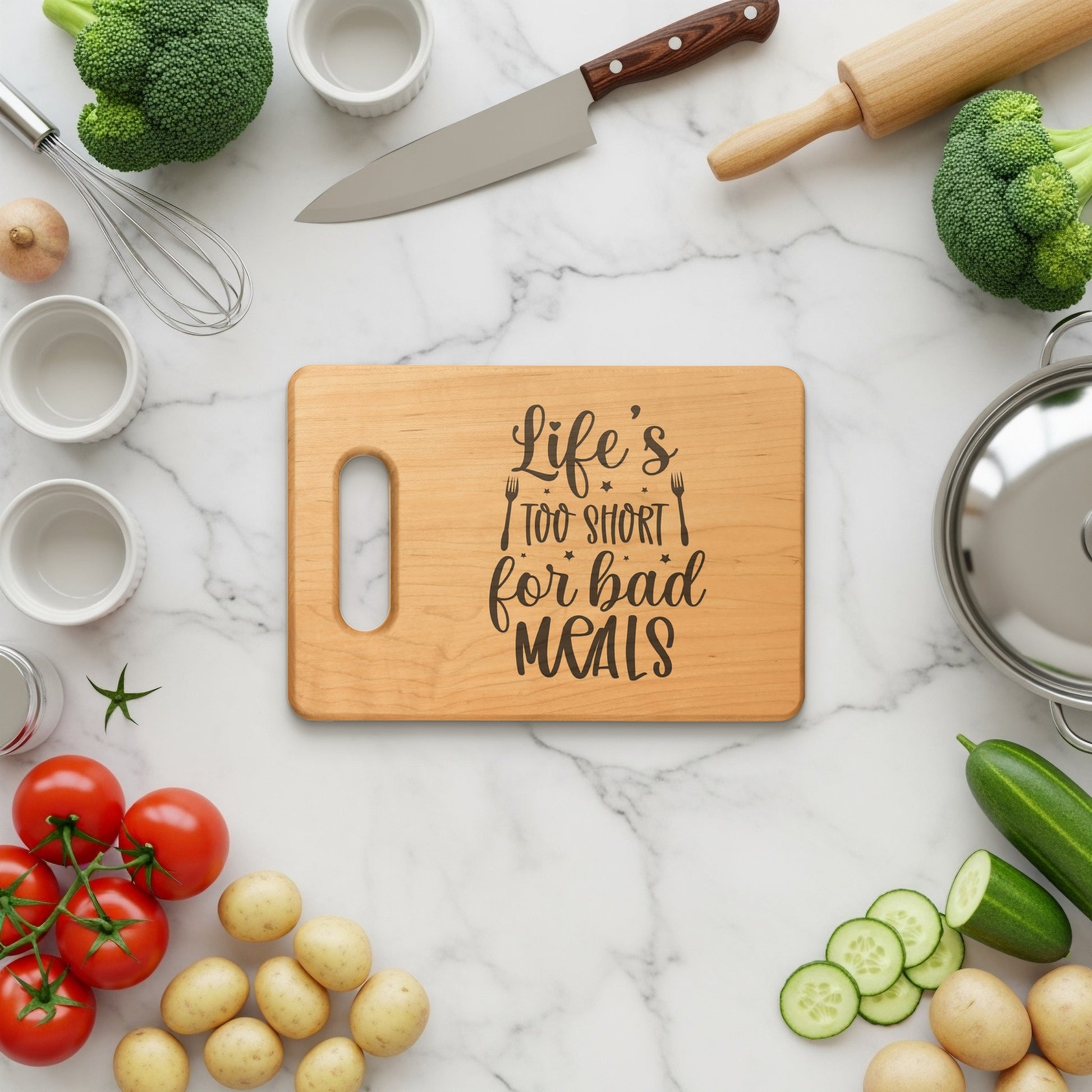 Wooden cutting board with "Life's too short for bad meals" engraving, surrounded by vegetables and kitchen tools.