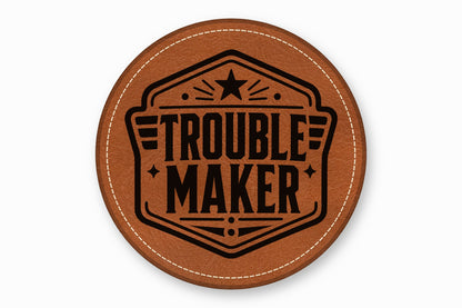 Round brown leather patch with white stitched border and black stamped text reading Trouble Maker.