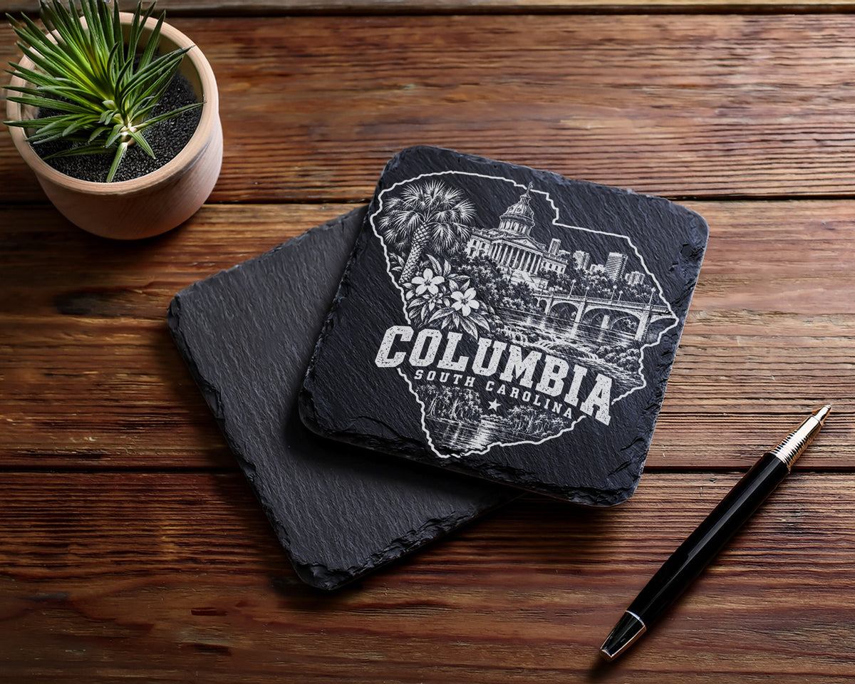 Two square black slate coasters with an engraved Columbia South Carolina design on a wooden table.