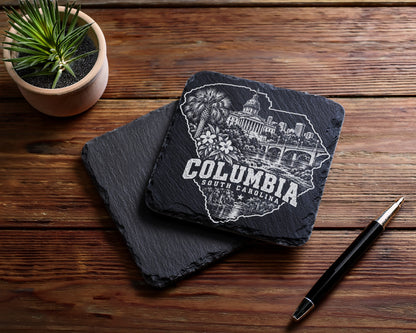 Two square black slate coasters with an engraved Columbia South Carolina design on a wooden table.