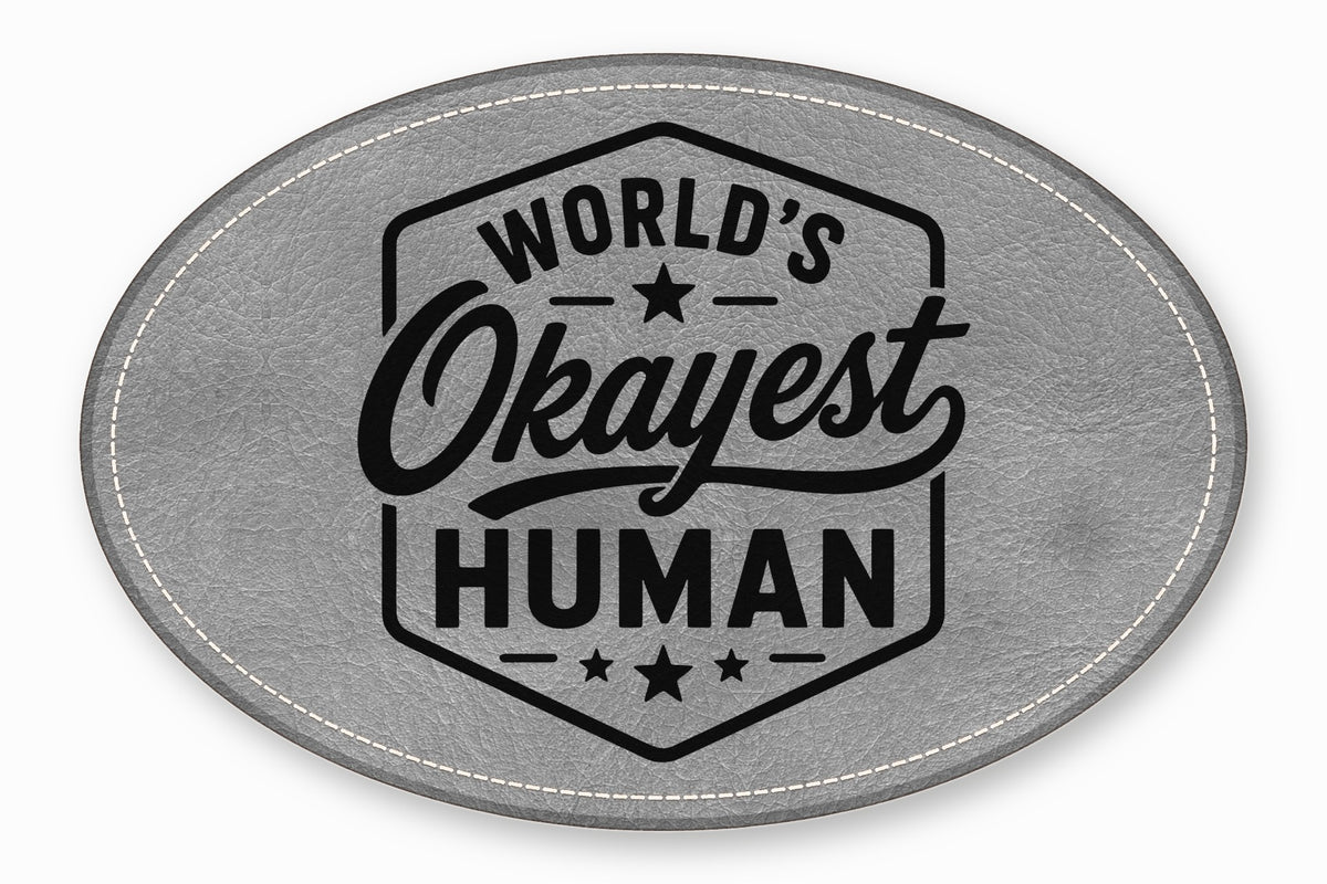 Oval gray leather patch with white stitching and the black text World's Okayest Human.