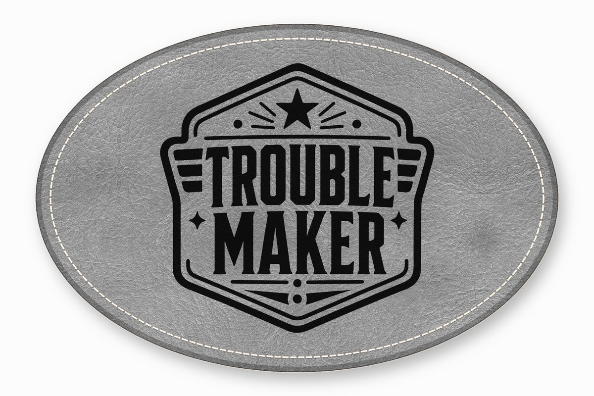 An oval grey leather patch with white stitched edges and a black Trouble Maker emblem.
