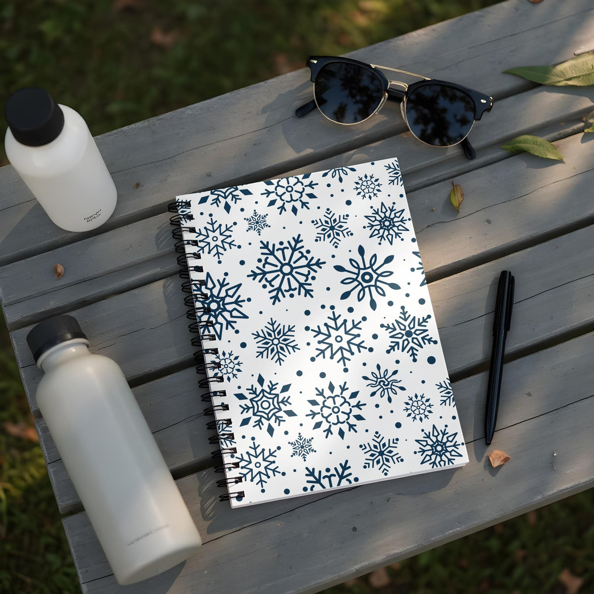 Spiral notebook with snowflake pattern and two water bottles on a wooden surface.