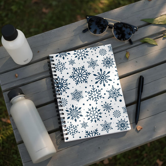 Spiral notebook with snowflake pattern and two water bottles on a wooden surface.