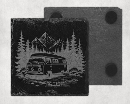 Slate coaster with etched design of a camper van parked in a forest with mountains.