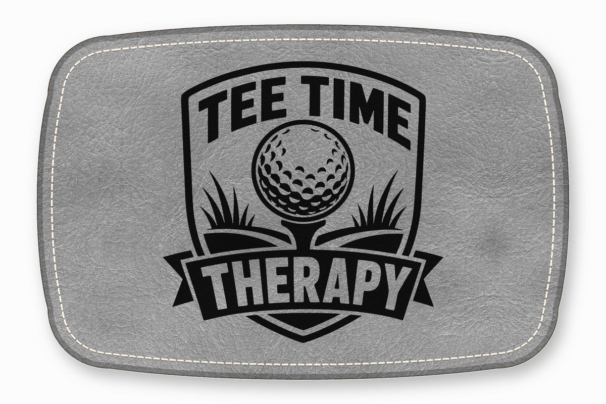 A grey leather patch with white stitched borders and a black engraved golf emblem reading Tee Time Therapy.