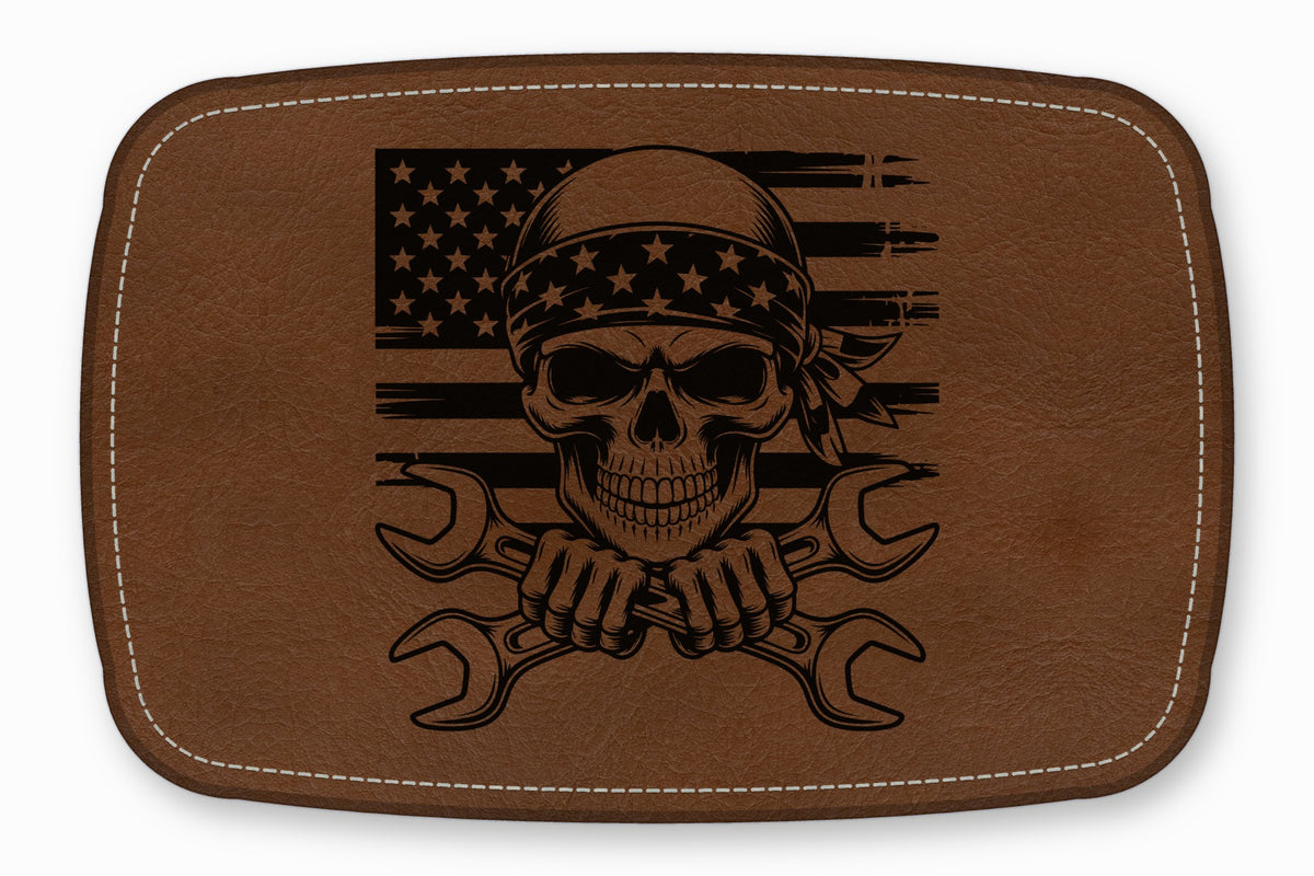 Brown leather patch with rounded corners featuring a black engraved skull wearing a bandana over crossed wrenches and an American flag.