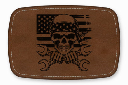 Brown leather patch with rounded corners featuring a black engraved skull wearing a bandana over crossed wrenches and an American flag.