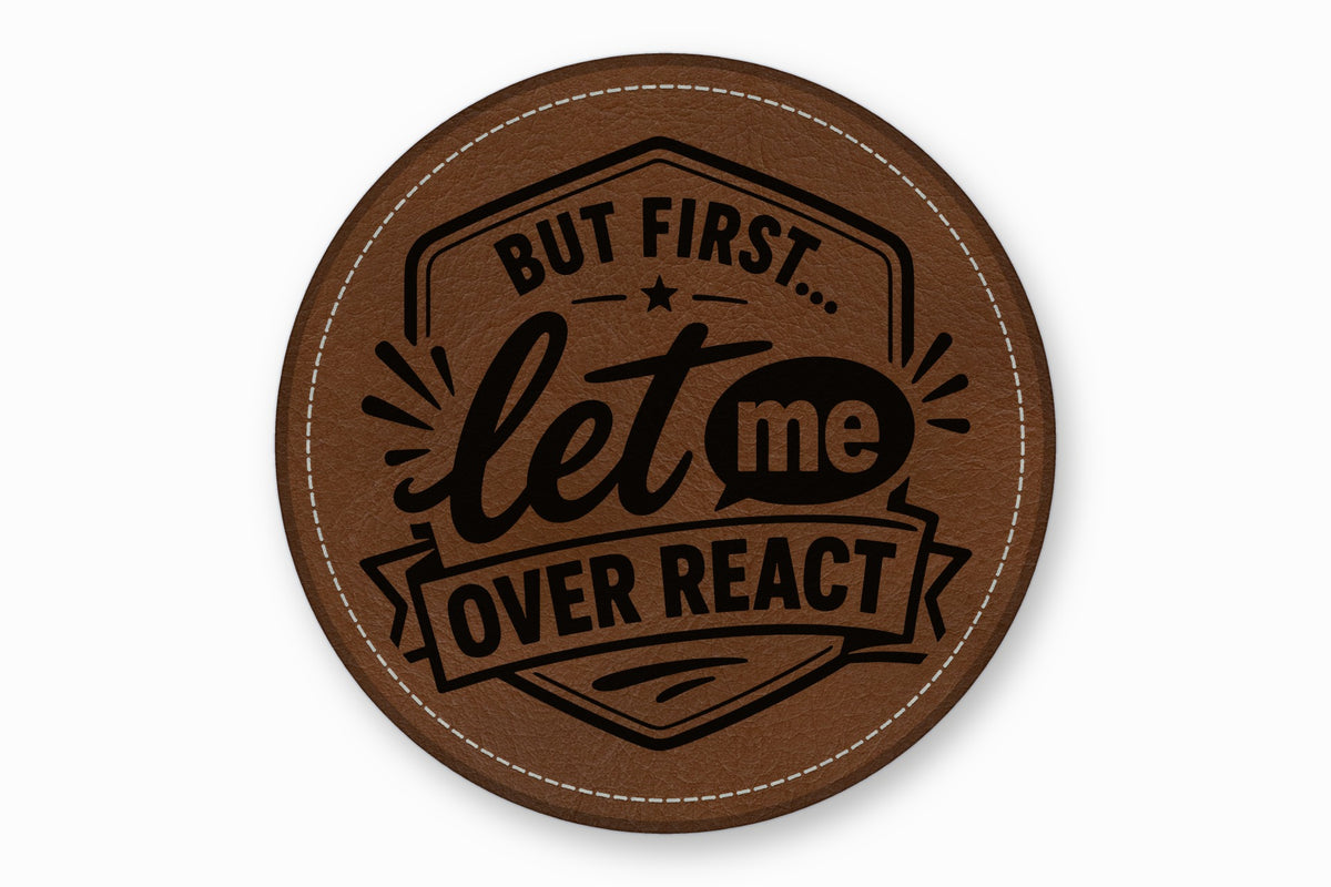 Round brown leather patch with white stitched edge and black engraved text reading, BUT FIRST... let me OVER REACT.