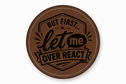 Round brown leather patch with white stitched edge and black engraved text reading, BUT FIRST... let me OVER REACT.