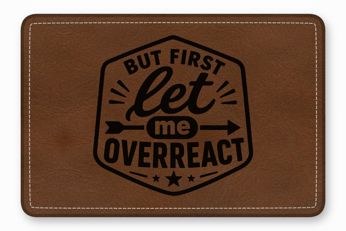Brown leather patch with white stitching and the engraved text But first let me overreact inside a black border.