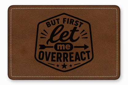 Brown leather patch with white stitching and the engraved text But first let me overreact inside a black border.