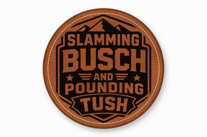 Round brown leather coaster with white stitched border, featuring a black mountain graphic and text reading SLAMMING BUSCH AND POUNDING TUSH.