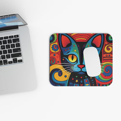 A colorful, abstract cat mousepad next to a silver laptop on a white desk.