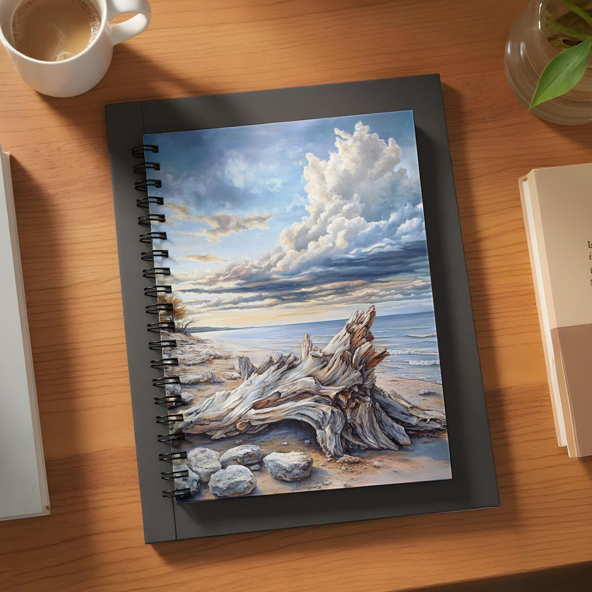 Spiral notebook with a painting of a driftwood on a beach and dramatic clouds.
