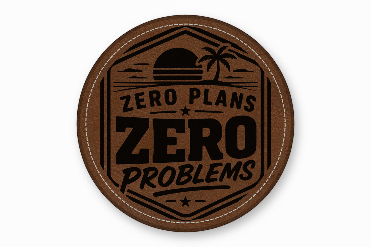 Round brown leather patch with white stitched border, featuring a black tropical sunset and text "ZERO PLANS ZERO PROBLEMS".