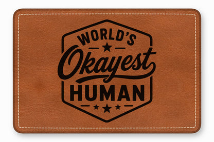 Brown leather patch with white stitched border and black text reading World's Okayest Human inside a badge.