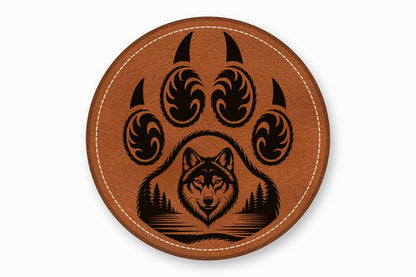 Round brown leather patch with white stitching featuring a black wolf head and forest inside a paw print.