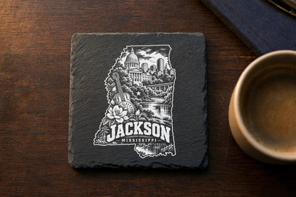 Square black slate coaster engraved with a Jackson, Mississippi skyline design featuring landmarks and text.