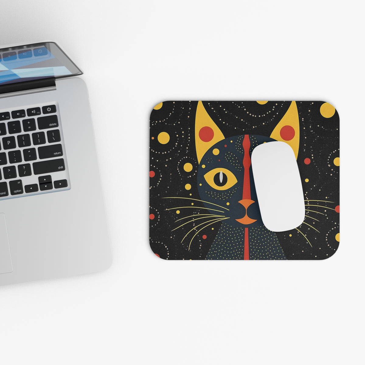 An abstract cat-themed mousepad with a white computer mouse next to a laptop on a white desk.
