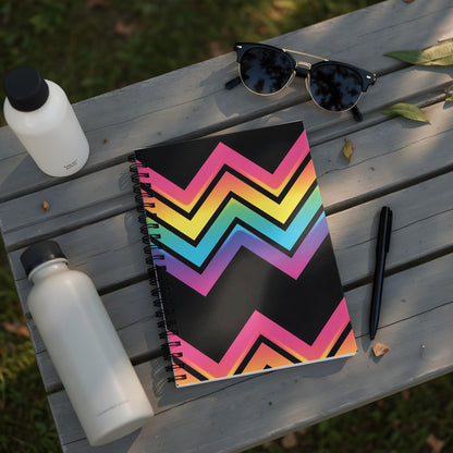 Spiral notebook with black cover featuring a rainbow zigzag pattern and items on a wooden table.